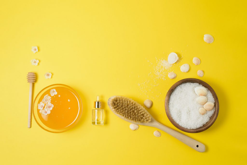 natural organic ingredients-sea salt, coffee scrub, honey and a hard body brush on a yellow background. home skin care for cellulite. concept of skin care, home Spa. the view from the top